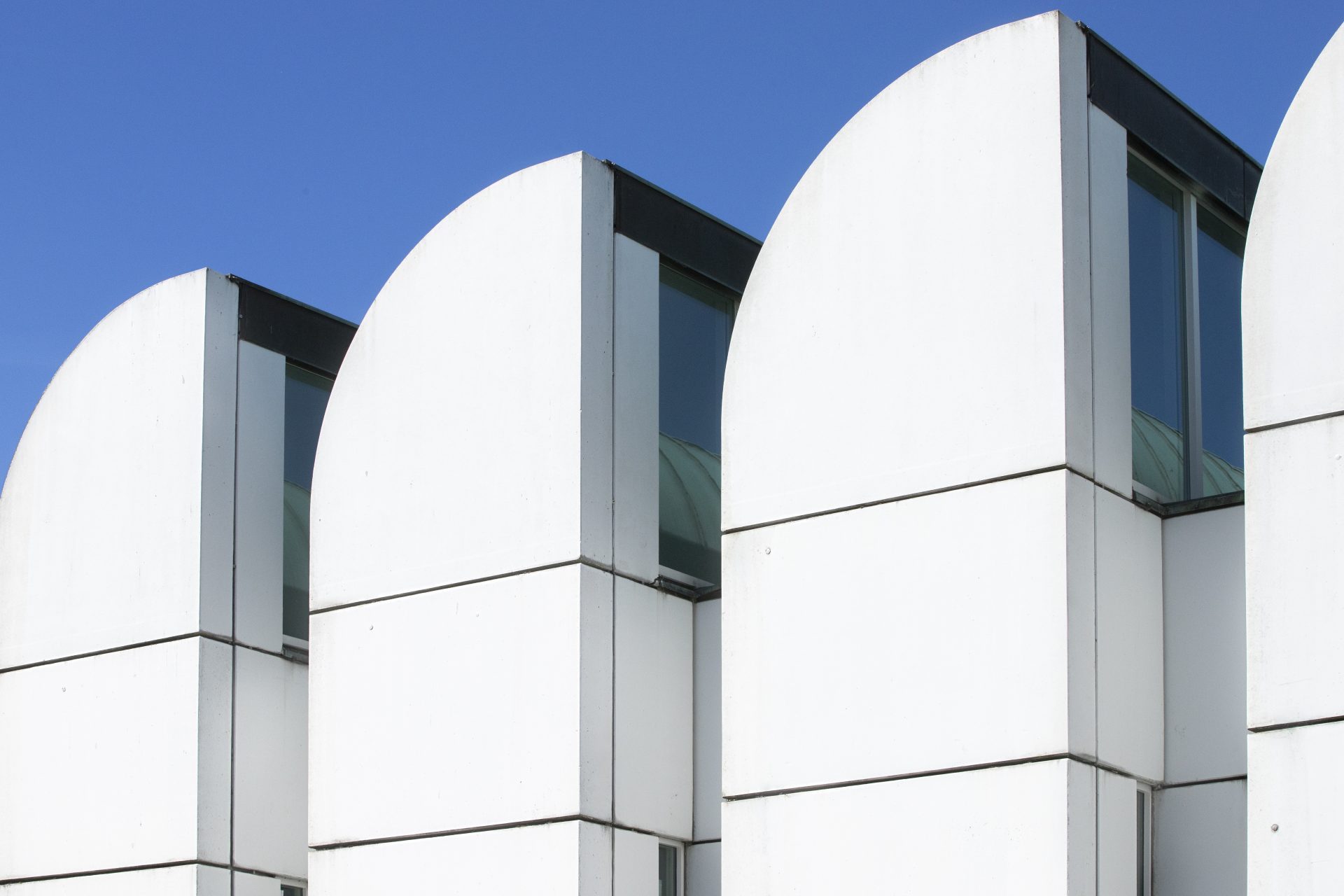Moderne Architektur mit geschwungenen weißen Fassadenelementen und Fenster im Kontrast zum blauen Himmel.