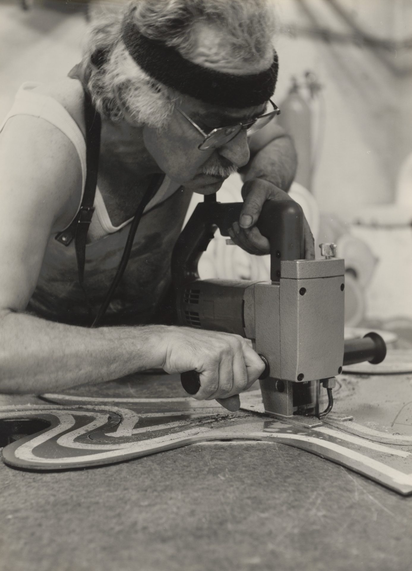 Ein älterer Handwerker arbeitet mit einer Stichsäge an einem Farbmuster auf einer Holzplatte.
